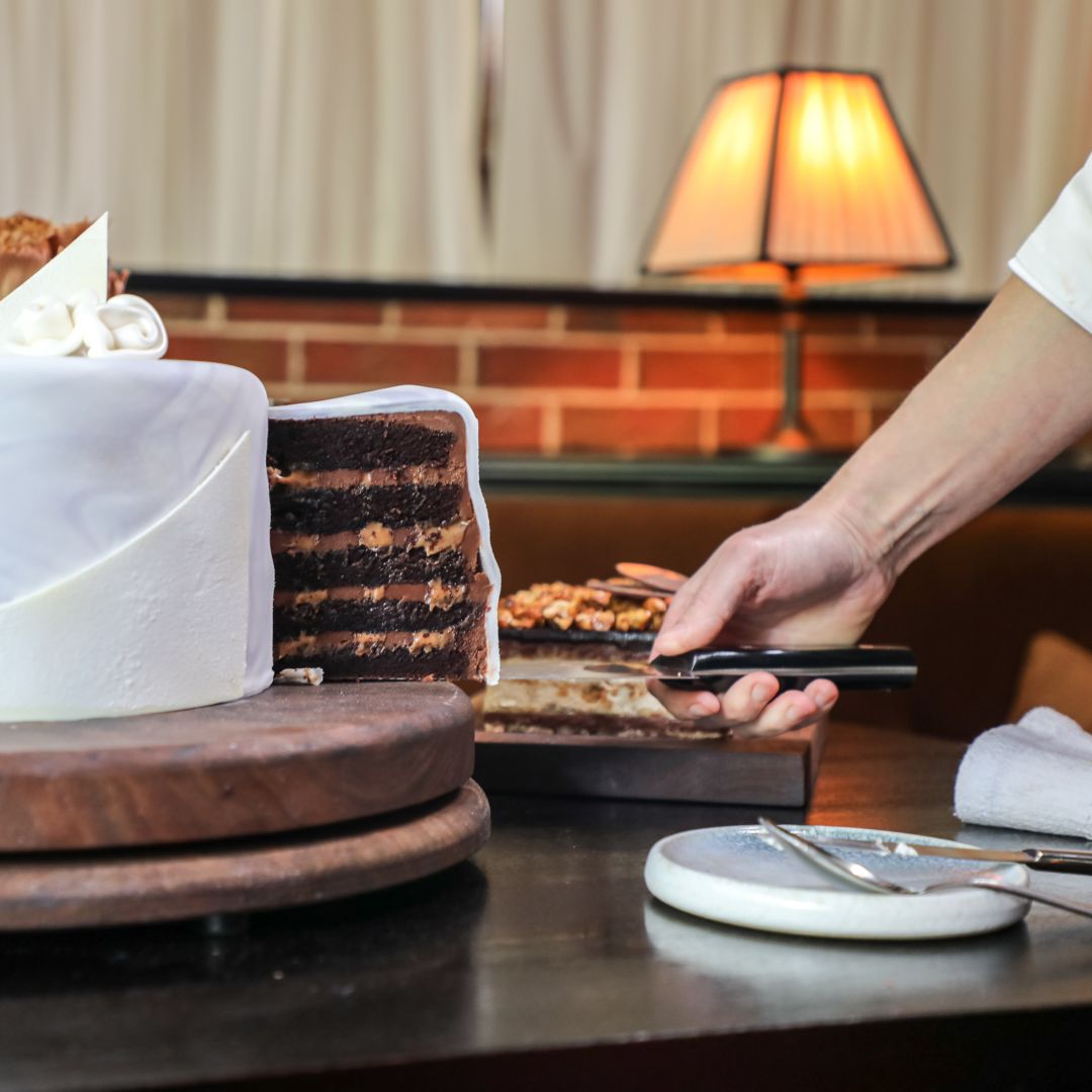 A waiter pours sauce on a plate of sliced  steak.